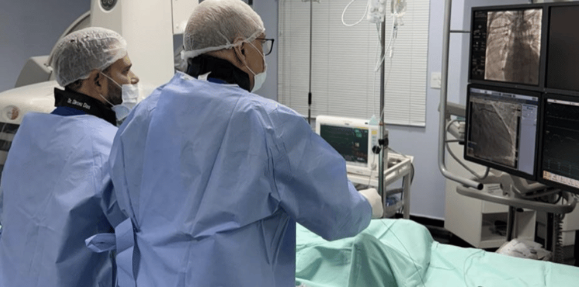 Médicos acompanham imagens em monitores durante procedimento percutâneo na sala de hemodinâmica